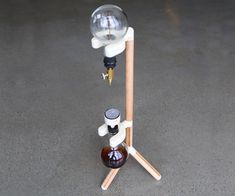 a glass bottle sitting on top of a tripod next to a wooden stick with a liquid dispenser in it