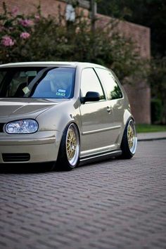 a silver car parked on the side of a road next to a brick wall and trees