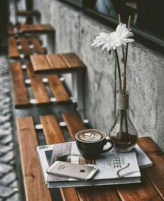 a cup of coffee sitting on top of a wooden table next to a vase filled with flowers