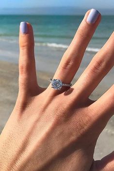 a woman's hand with a ring on it near the beach and water in the background