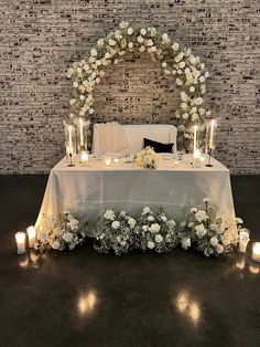 a table with candles and flowers on it in front of a brick wall behind the headboard