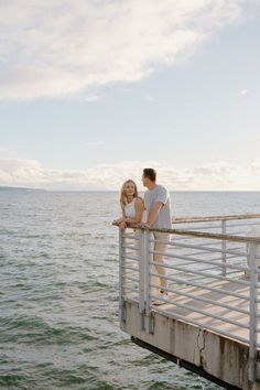 a man and woman standing on a pier next to the ocean