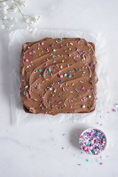 a cake with chocolate frosting and sprinkles next to a bowl of sprinkles