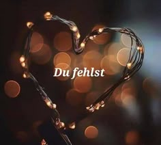 the words du fehlist written in front of a heart shaped string of lights