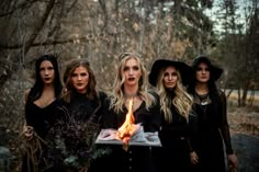 three women in witches costumes holding a tray with a cake on it while standing next to each other