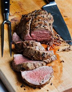 sliced meat sitting on top of a wooden cutting board next to a knife and fork