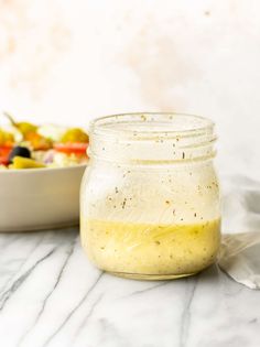 a glass jar filled with dressing next to a bowl of salad on a marble surface