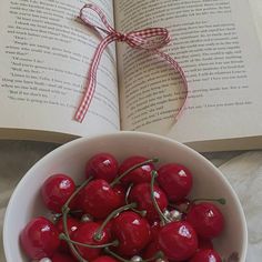 a bowl filled with cherries next to an open book