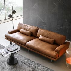 a brown leather couch sitting in a living room next to a glass vase and lamp