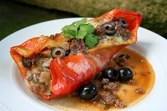 a white plate topped with stuffed peppers covered in sauce and black olives on top