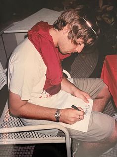 a man sitting in a chair holding a piece of paper and writing something on it