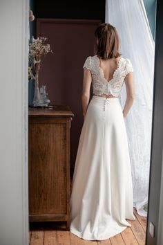 a woman standing in front of a mirror wearing a white dress and looking at her back