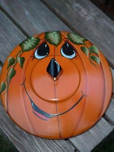 an orange painted pumpkin sitting on top of a wooden bench with eyes and leaves drawn on it