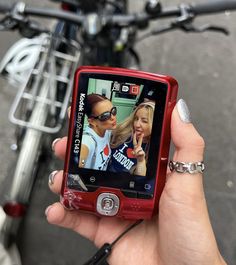 a person holding a red cell phone in front of a bike with two girls on it