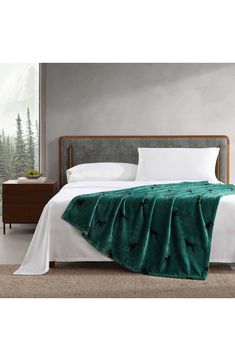 a bed with a green blanket on top of it next to a night stand and nightstand