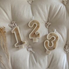 three candles with numbers on them sitting on a white surface next to dried flowers and twigs