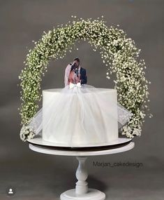 a bride and groom are standing on top of a white wedding cake with greenery