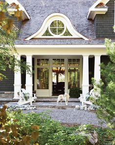 two white dogs are standing in front of a house with black shingles and windows