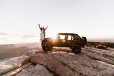 a man and woman standing on top of a rock with their arms in the air