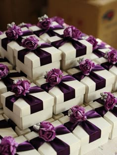 several white boxes with purple ribbons and flowers on them are stacked up in the shape of cubes