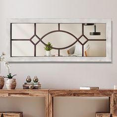 a mirror hanging on the side of a wall above a wooden table with vases