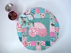 a pink and blue patchwork placemat with an elephant design on it, next to a measuring cup