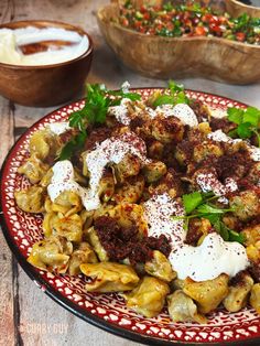 a red and white plate topped with pasta covered in sauce next to bowls of salad