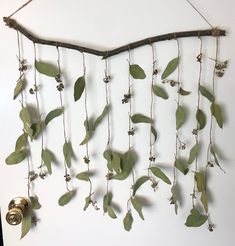 a wind chime with green leaves and flowers hanging from it's side on a white wall