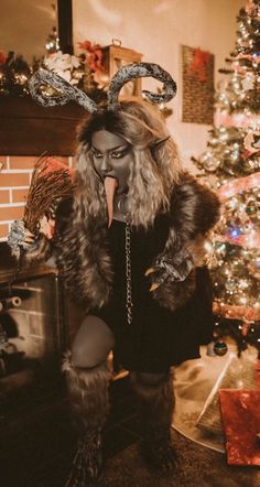 a woman dressed as a demon in front of a christmas tree with her tongue out