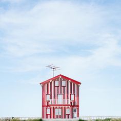 a red and white house sitting on top of a lush green field next to the ocean