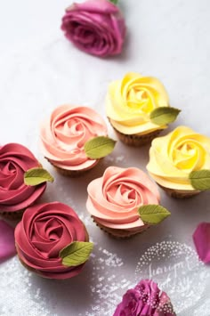 cupcakes with pink, yellow and red frosting are arranged on a table