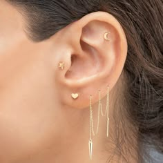 a close up of a person's ear wearing gold earrings with dangling chains and stars