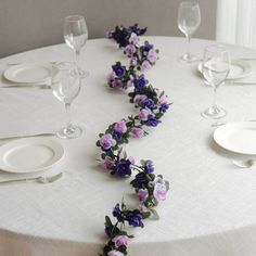 the table is set with white plates and purple flowers