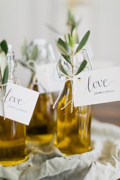 two bottles with olives and love tags on them sitting on a cloth covered table