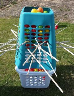 a blue basket filled with lots of fruit on top of a grass covered field next to sticks