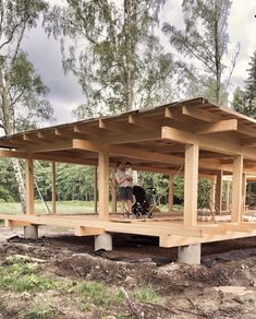 two people standing on top of a wooden structure in the middle of a field next to trees