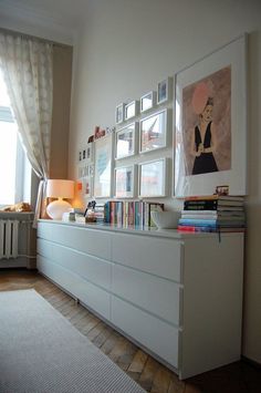 a white dresser sitting next to a window filled with books and pictures on top of it