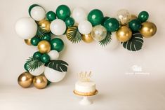 a cake sitting on top of a white table next to balloons and palm leaf decorations