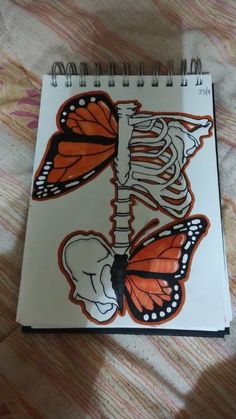 a spiral notebook with an image of a skeleton and butterfly on the cover, sitting on a bed