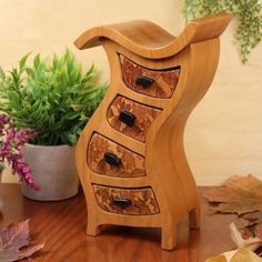 a wooden vase with drawers sitting on top of a table next to some leaves and flowers