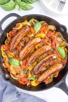 sausages and peppers in a skillet with basil leaves on the table next to it