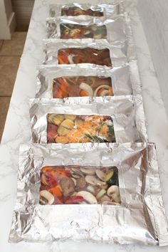 four trays filled with food sitting on top of a counter covered in aluminum foil