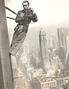 an old photo of a man holding a camera up to the side of a tall building