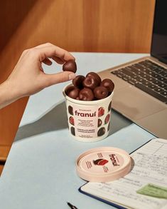 a cup of chocolate covered doughnuts sitting on a desk next to a laptop