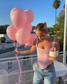 a woman holding pink balloons and a cake