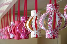 pink and white paper lanterns hanging from the ceiling in a room with red ribbons on them