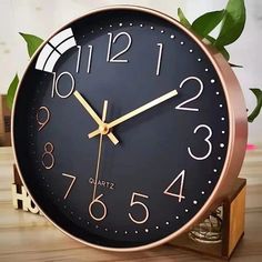 a black and gold clock sitting on top of a wooden table next to a potted plant