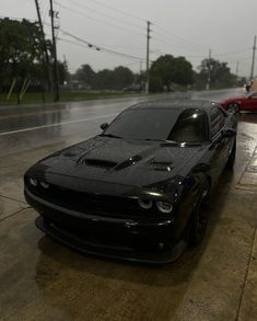 a black car parked on the side of a wet road next to a red car