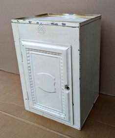 an old white cabinet sitting on top of a floor next to a wall with a door