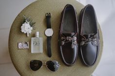 a pair of brown shoes sitting on top of a table next to sunglasses and a watch